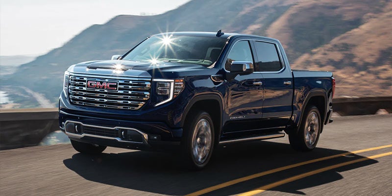 This image shows a GMC full-size pickup truck driving along a scenic mountain road