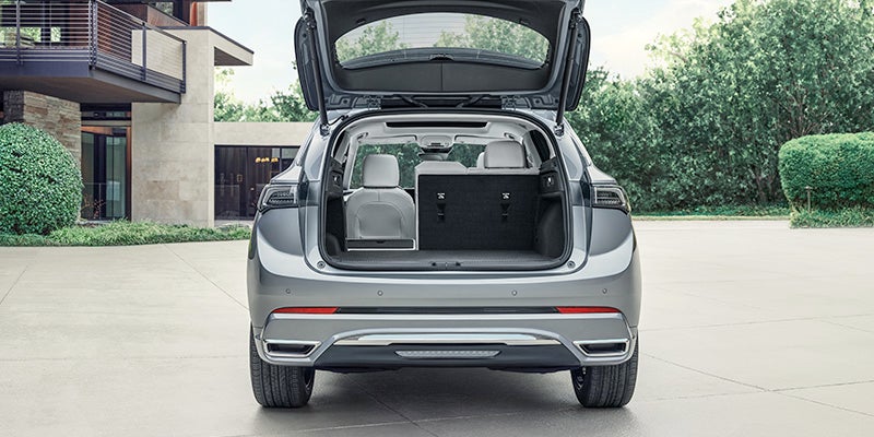 Rear view of a silver SUV parked in a residential driveway with the liftgate open, showing a spacious cargo area