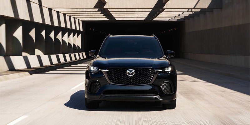 Black Mazda CX-series SUV parked in a modern concrete parking structure, shown from a front three-quarter angle with black alloy wheels and a bold front grille.