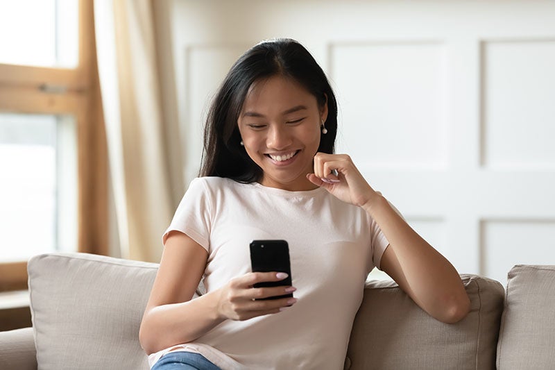 Happy young asian ethnic woman looking at smart phone screen.