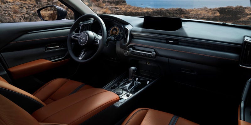 Wide view of a Mazda vehicle interior featuring premium brown leather seats, a multifunction steering wheel