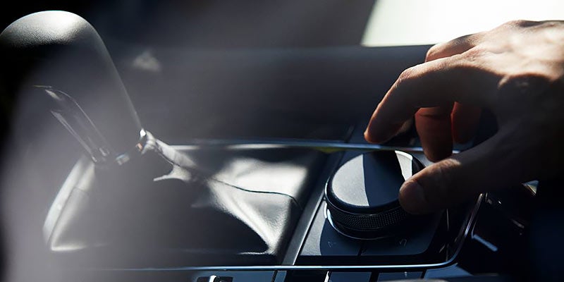 Close-up of a hand operating the rotary infotainment control knob on a Mazda vehicle's center console
