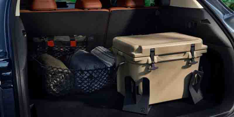 Open cargo area of a Mazda SUV containing outdoor gear, including a large hard-sided cooler, storage bags, and equipment secured with cargo nets