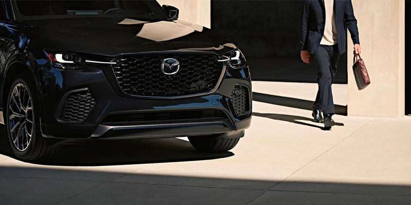Close-up of a black Mazda SUV showcasing the signature front grille, LED headlights, and front wheel in a modern architectural setting.