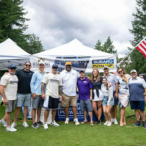 Group of people posing outdoors in front of a Subaru Puyallup event tent.