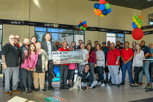 Group of dealership employees posing indoors with a donation check and a dog.