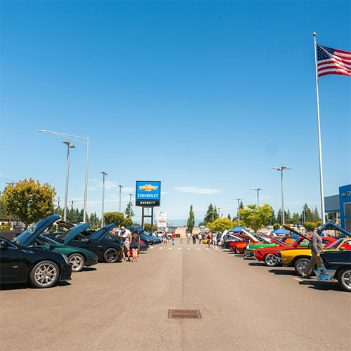 Classic cars displayed at a dealership car show under a clear blue sky.
