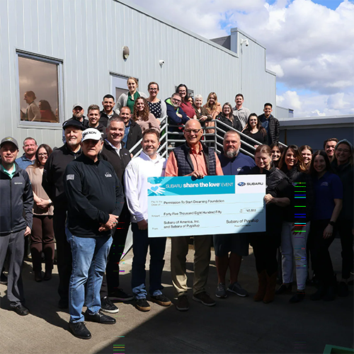 Dealership team gathered outside holding a large donation check.