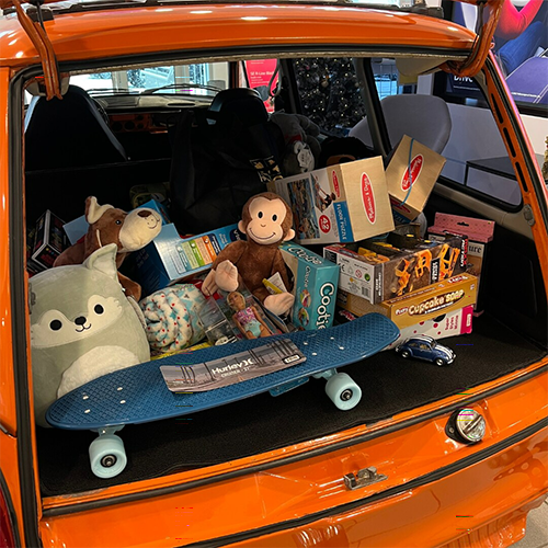 Open trunk of an orange car filled with toys, boxes, stuffed animals, and a skateboard