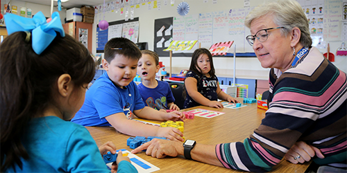 Teacher assisting young students during a classroom learning activity.