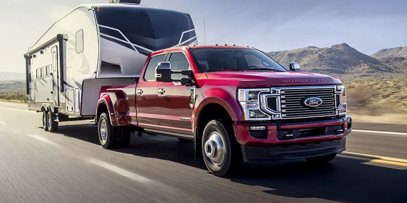 Red Ford Super Duty dually truck hauling a large fifth-wheel camper on a highway, with mountains in the background.