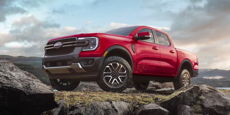 A red Ford Ranger pickup truck with black accents, parked on a rocky, moss-covered ridge overlooking a valley.