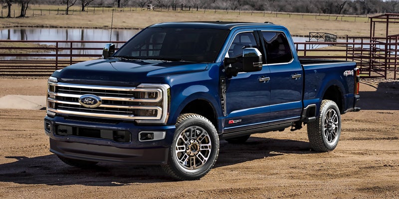 A dark blue Ford F-250 pickup truck with chrome accents, angled on a dirt road beside a pond.