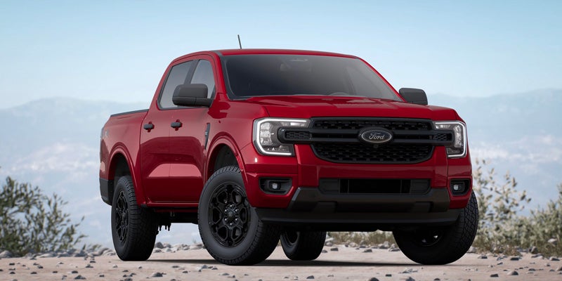 Red Ford Ranger pickup truck with black wheels, parked on a dirt road