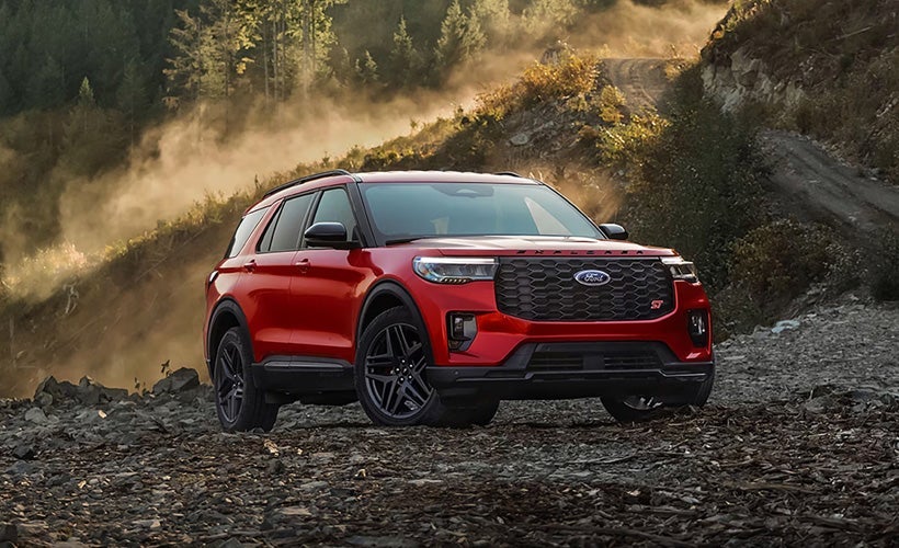 Red Ford SUV driving off-road on a rocky dirt trail in a forest with dust clouds and sunlight in the background.