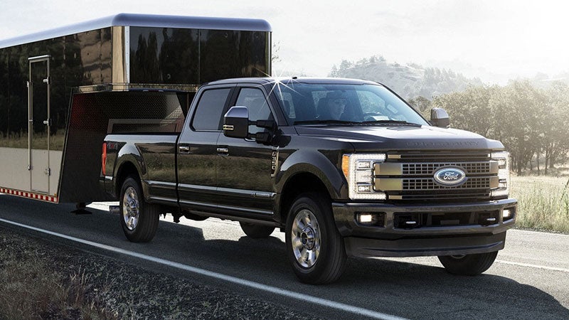 A black Ford F-Series Super Duty truck towing a shiny black enclosed trailer on a rural road.