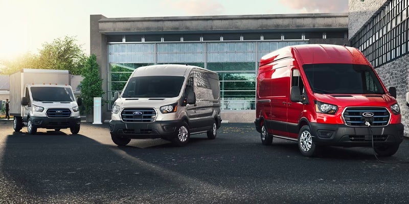 Three Ford E-Transit vans in white, silver, and red parked in a lineup in front of a building