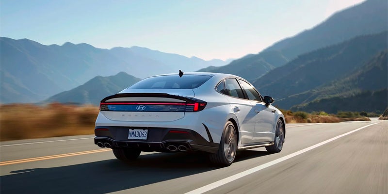 Rear view of a Hyundai Sonata moving right on a mountain road with blurred background.