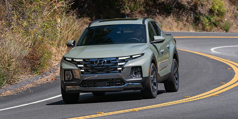 Hyundai Santa Cruz truck, with black cladding, driving around a sharp curve on a winding road.