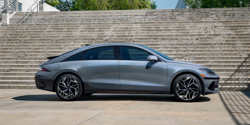 electric sedan with geometric wheels is parked on concrete next to large rough-hewn concrete steps.