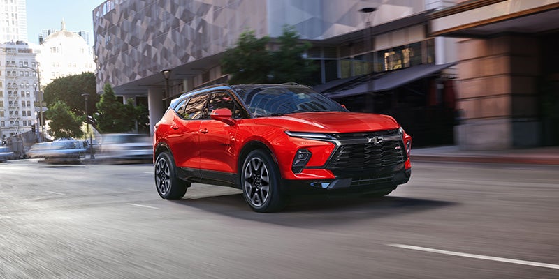 A red Chevrolet Blazer RS drives on a city street, with buildings in the background.