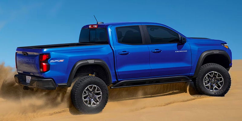 Blue Chevrolet Colorado ZR2 pickup truck driving across sandy terrain.