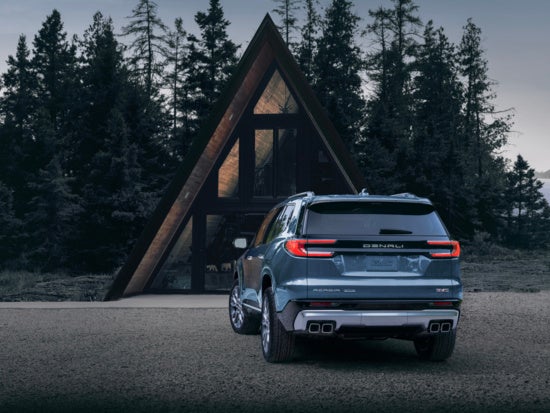 Blue GMC Acadia SUV parked on a gravel road, with trees in the dark background.