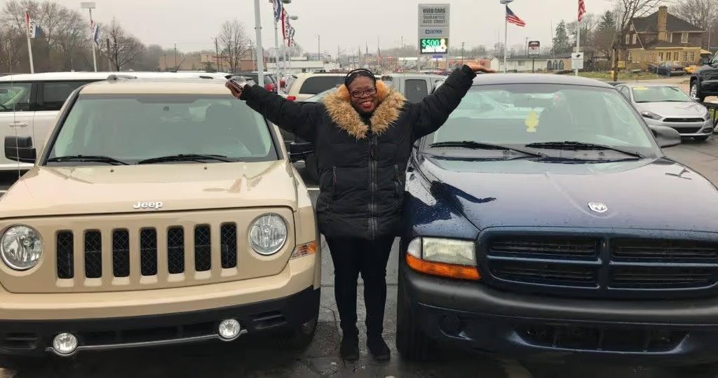 Customer celebrating with arms raised beside their new vehicle on the Cueter lot