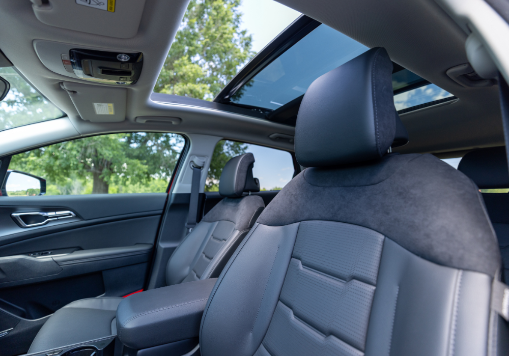 2026 Kia Sportage interior. The seats are black and the sunroof is open above them.