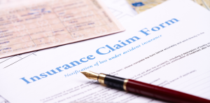 Close-up of an “Insurance Claim Form” partially covered by a fountain pen and an ID card, representing the process of filing a claim after an accident