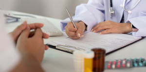 Doctor writing on medical form during consultation, with prescription bottles and patient nearby