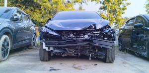 Front view of a severely damaged black car with a crushed bumper and hood parked between two other vehicles after a collision