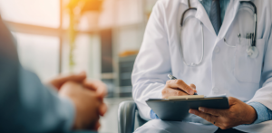 Doctor writing notes while listening to a patient during a mental health consultation