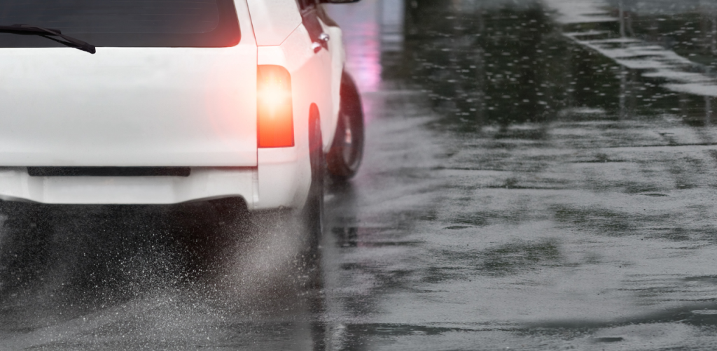White SUV skidding on a wet road, leaving a trail of water spray, highlighting the risk of accidents and the need for a car accident lawyer