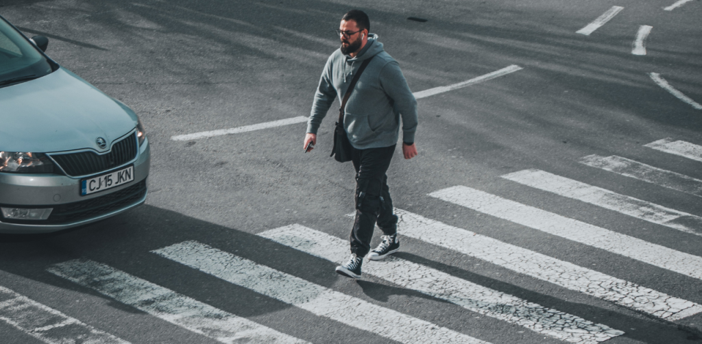 Man in a hoodie crossing a street as a car approaches
