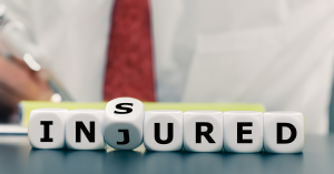 White dice spelling out "INSURED" with one die flipped to change the word to "INJURED," indicating a transition from insured to injured