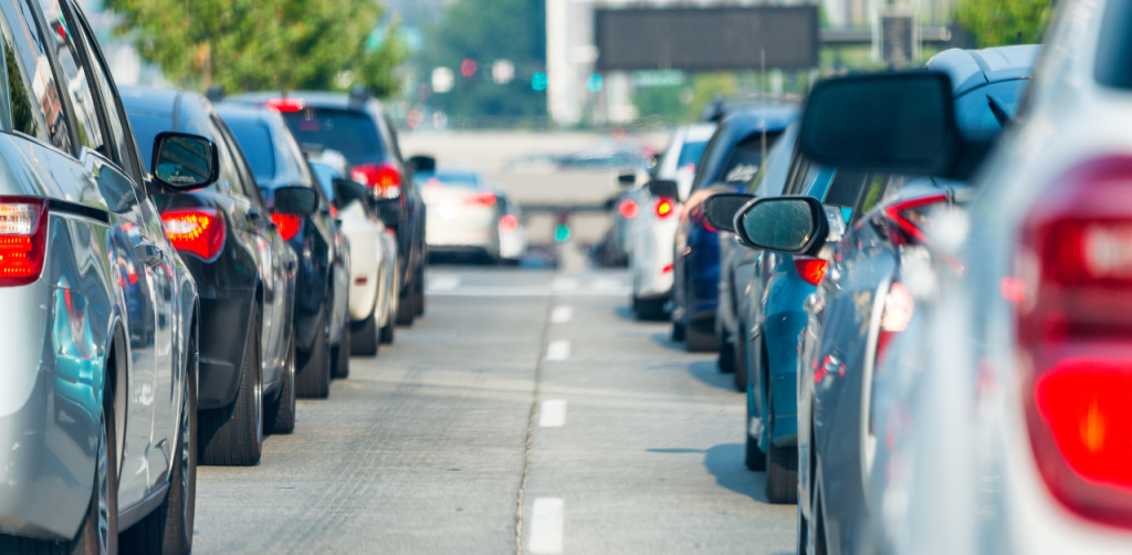 Cars sit in heavy traffic on a city street with brake lights glowing and lanes filled in both directions