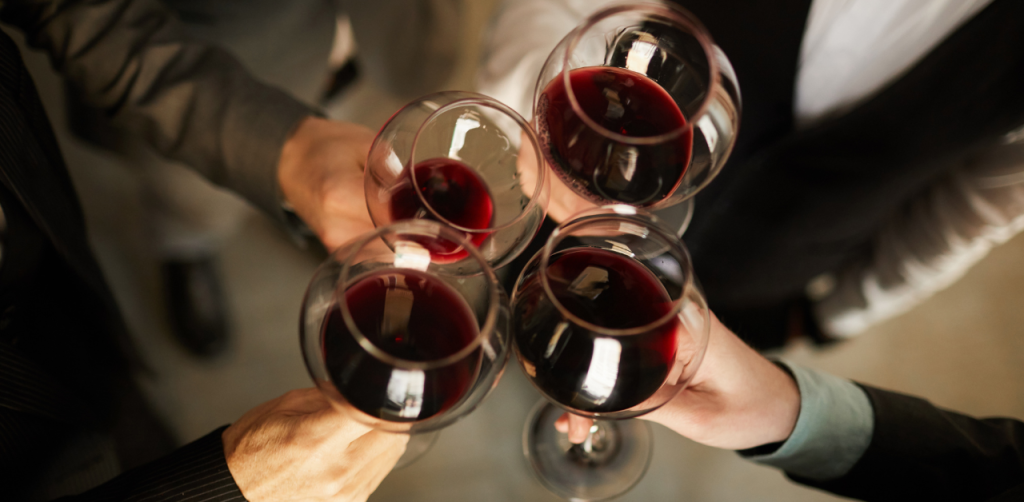 Group toasts with glasses of red wine, dressed in formal attire, celebrating at a social event