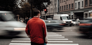 Man in red jacket waits at a crosswalk during heavy traffic with a red light, emphasizing safe street crossing