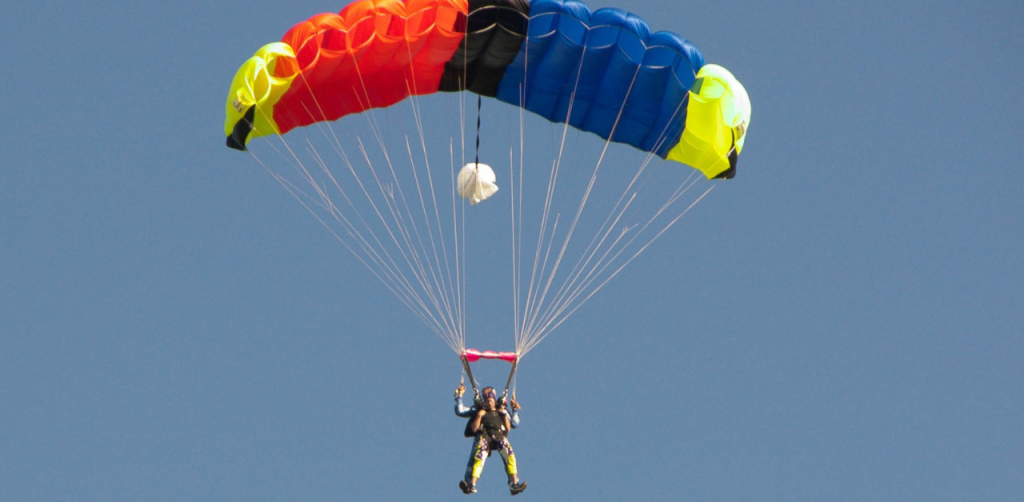 A skydiver glides through the air with a vibrant rainbow-colored parachute against a clear blue sky