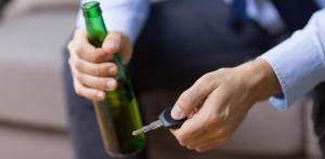 A man holds a beer bottle in one hand and car keys in the other, symbolizing drunk driving danger