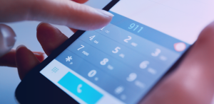 Close-up of a smartphone keypad with 911 entered on the screen as a finger hovers above the dial pad