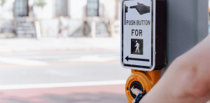 Hand pressing pedestrian crossing button on traffic signal, promoting safe street crossing and walk signal activation