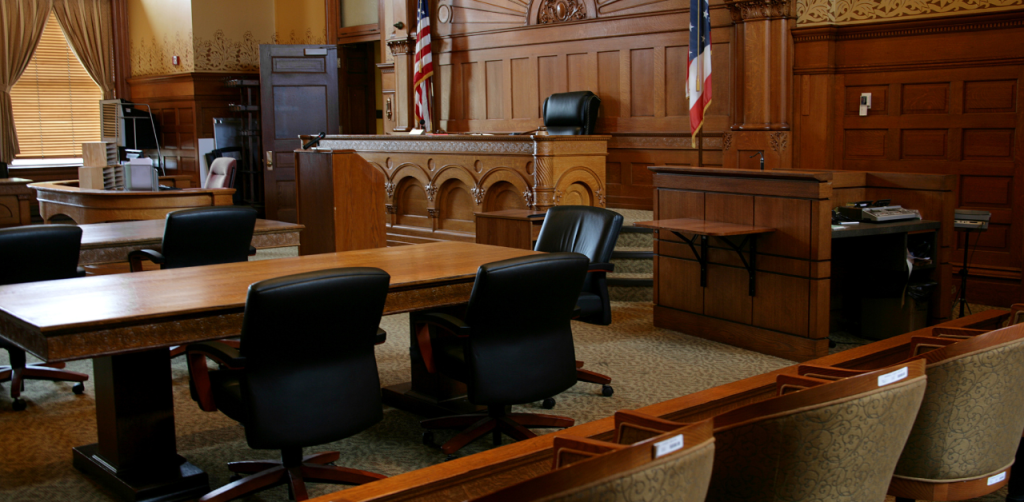Empty courtroom with wooden furniture, judge’s bench, and flags, awaiting a legal trial or hearing