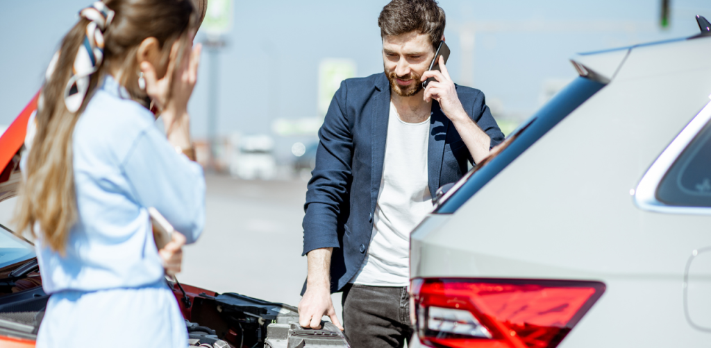 A man on his phone standing near two cars involved in a collision, with a woman holding her head in concern