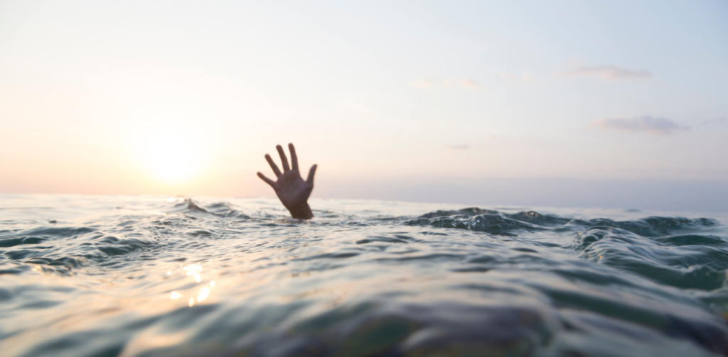 A hand reaching out of the ocean water at sunset, with sunlight reflecting on the waves and the horizon glowing in warm tones