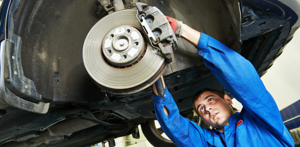 A mechanic in a blue uniform working on the brake system of a car lifted on a vehicle hoist