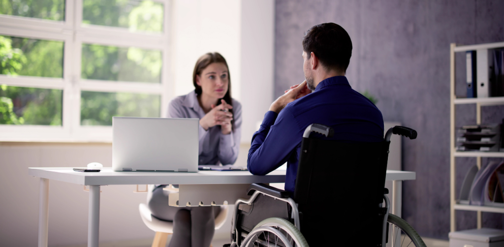 Man in a wheelchair meets with a woman in an office, discussing a possible legal settlement claim
