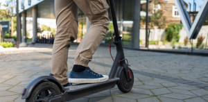 Close-up of a person in tan pants and sneakers riding an electric scooter on a paved urban pathway