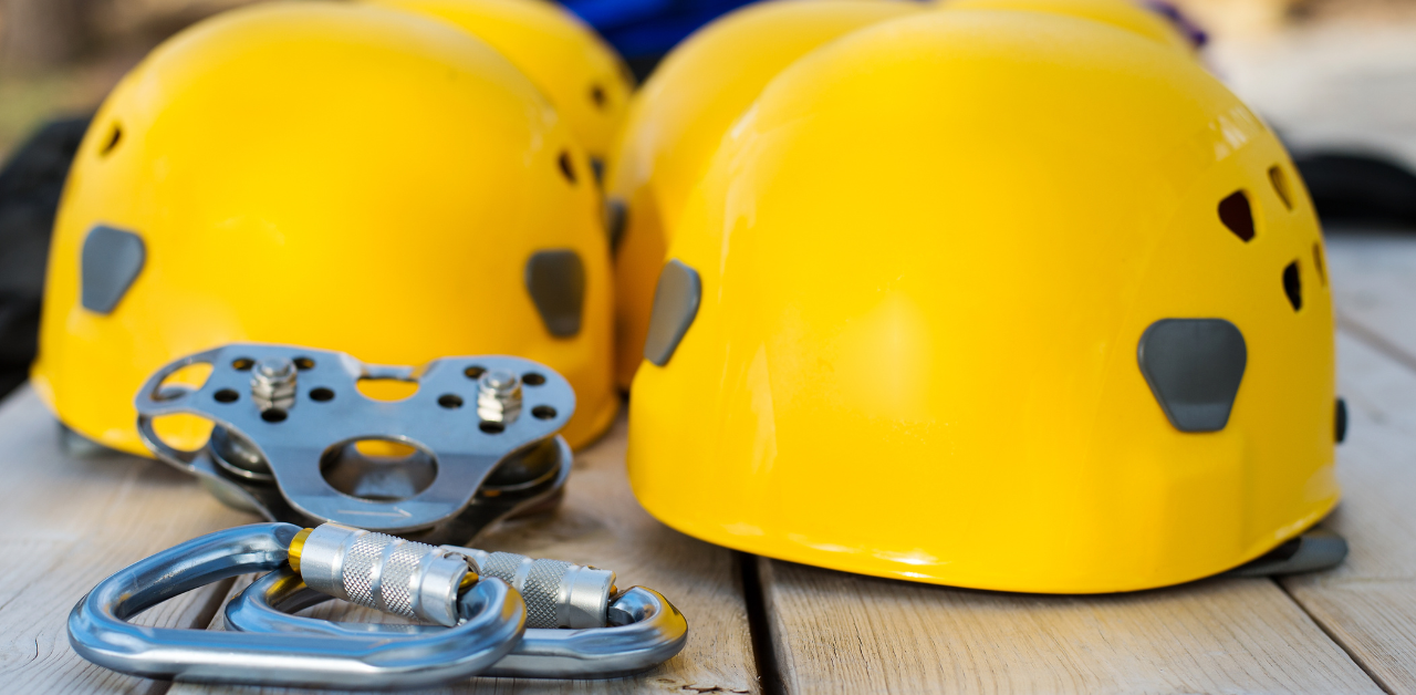Group of bright yellow safety helmets, carabiners, and pulley gear laid out on a wooden surface, representing essential protective equipment for zip lining or rope-based adventure activities